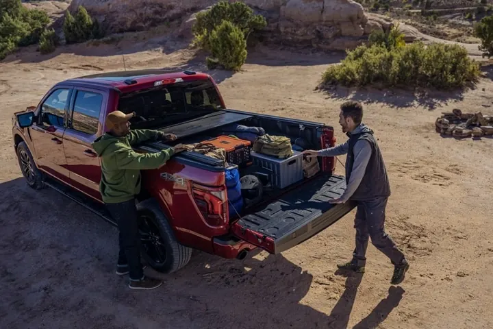 Two people unloading gear from a red pickup truck on a gravel road